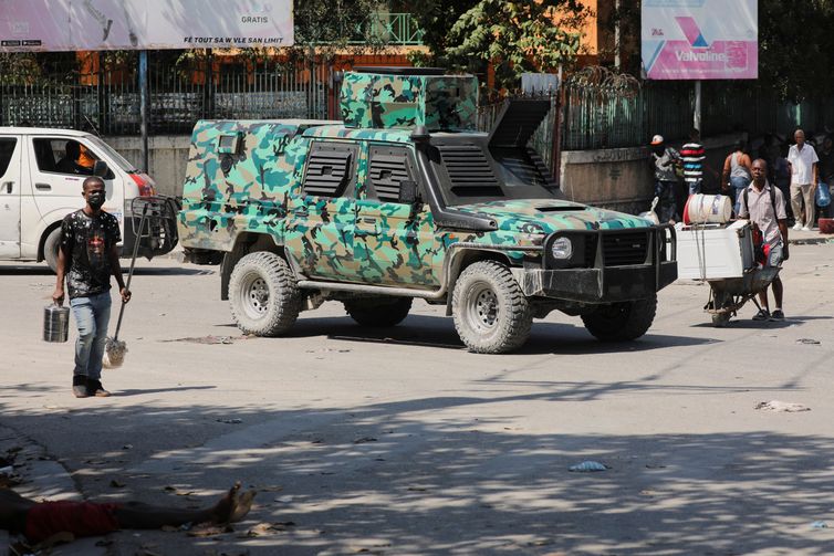 SENSITIVE MATERIAL. THIS IMAGE MAY OFFEND OR DISTURB  A man walks near a body while a military vehicle patrols after the government declared a state of emergency amid violence, in Port-au-Prince, Haiti, March 4, 2024. REUTERS/Ralph Tedy Erol