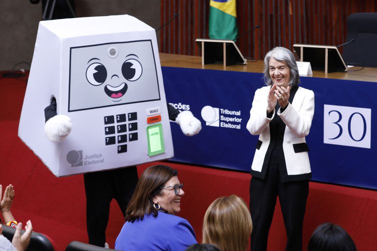 Alejandro Zambrana/Secom/TSE Brasília (DF), 01/05/2026 - Mascote do TSE e a ministra Cármen Lúcia durante cerimônia de comemoração aos 30 anos da Urna Eletrônica. Foto: Alejandro Zambrana/Secom/TSE